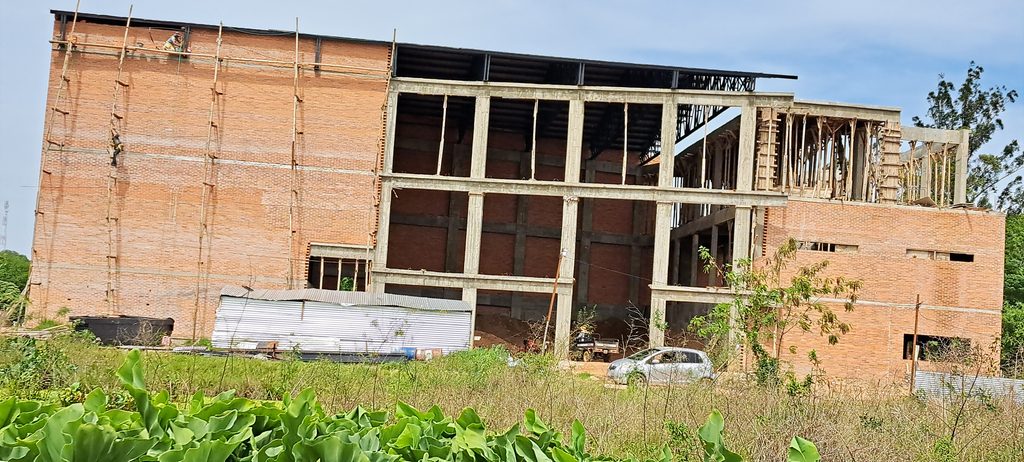 Alltag in Paraguay: Mehrstöckige Baustelle mit Ziegelwänden, Betonstützen und einem Gerüst aus Holzstangen.